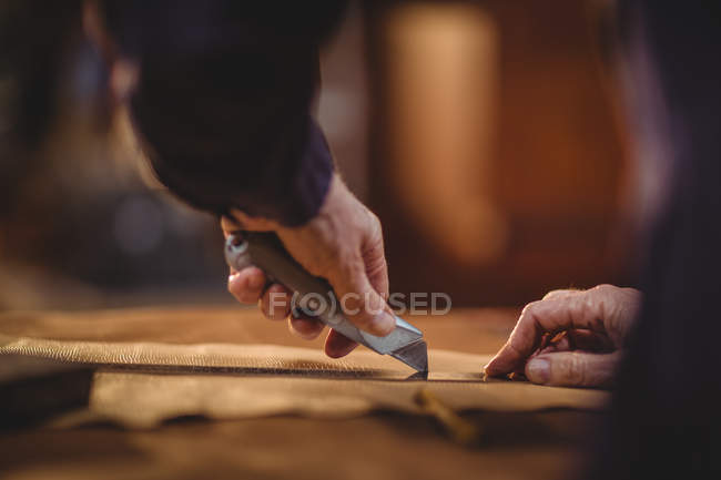 Manos de zapatero cortando un trozo de cuero en el taller - foto de stock