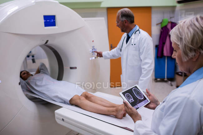 Médico mirando la resonancia magnética cerebral en la tableta digital y paciente entrando en la máquina de exploración de resonancia magnética en el hospital - foto de stock