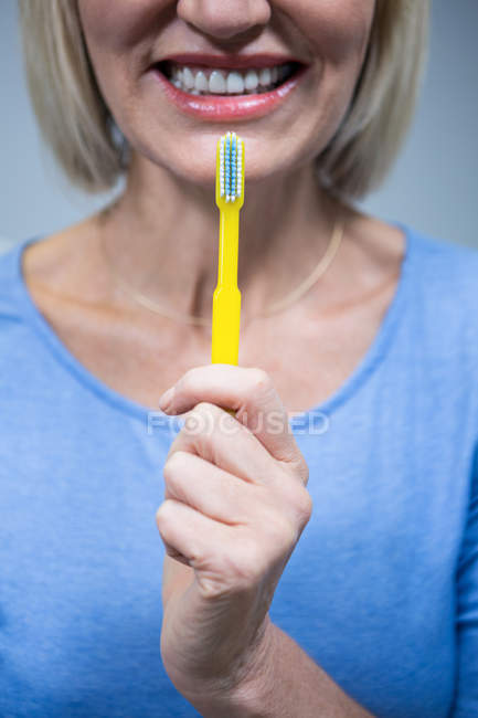 Partie médiane d'une femme souriante tenant une brosse à dents — Photo de stock