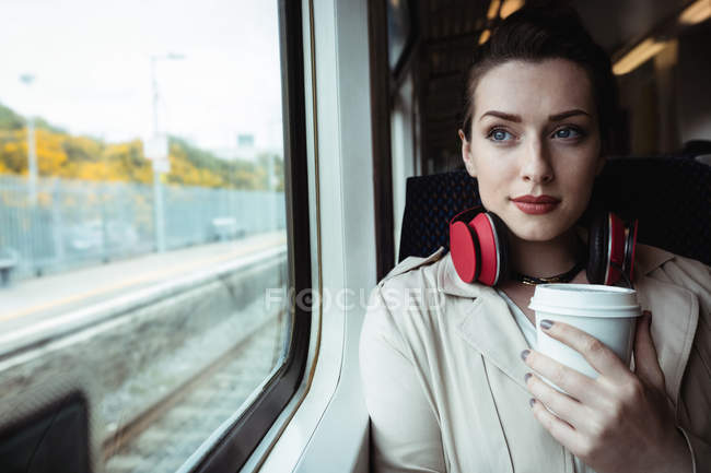 Young woman holding disposable cup by window in train — Stock Photo