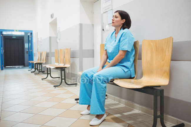 Traurige Krankenschwester sitzt auf Holzstuhl im Krankenhausflur — Stockfoto