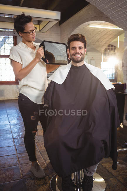 Sorrindo cabeleireiro feminino mostrando o homem seu corte de cabelo no espelho no salão — Fotografia de Stock
