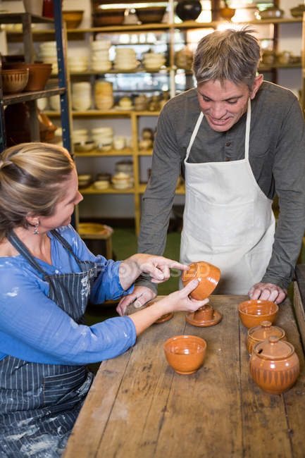 Alfareros sonrientes revisando ollas en taller de cerámica - foto de stock