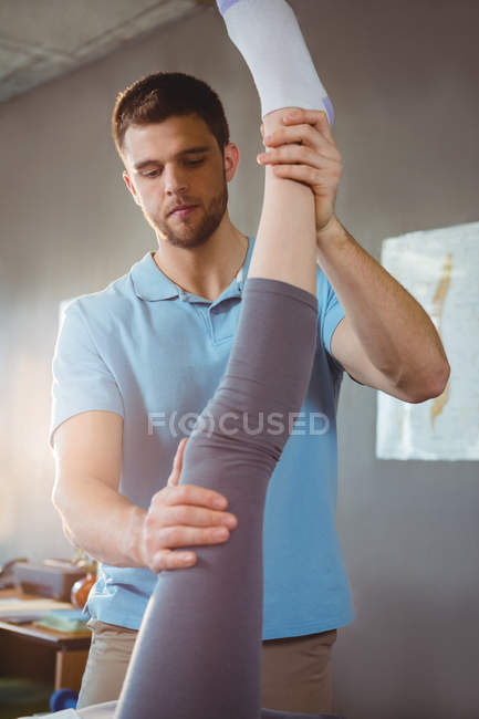Fisioterapeuta masculino dando masaje de piernas a paciente femenina en clínica - foto de stock