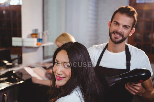 Portrait de femme souriante se faire sécher les cheveux avec sèche-cheveux au salon de coiffure — Photo de stock