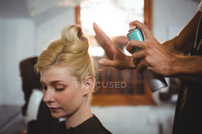 Hairdresser styling customers hair with spray in salon — Stock Photo