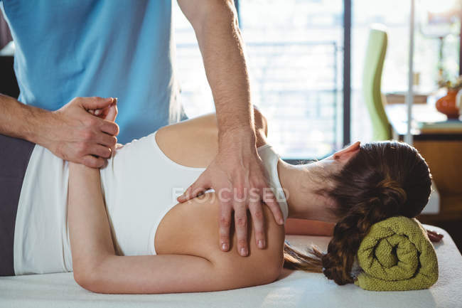 Мужской физиотерапевт делает массаж спины пациентке в клинике — стоковое фото