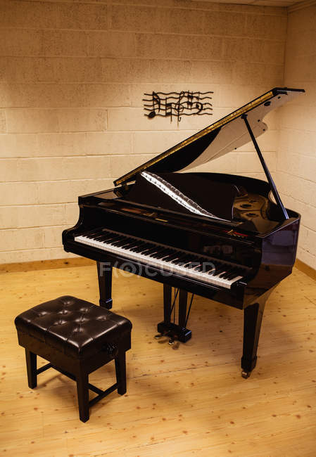 Piano y banco en el suelo de madera en una habitación - foto de stock