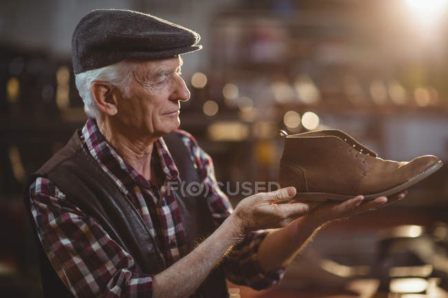 Oberschuhmacher mit Mütze begutachtet Schuh in Werkstatt — Stockfoto