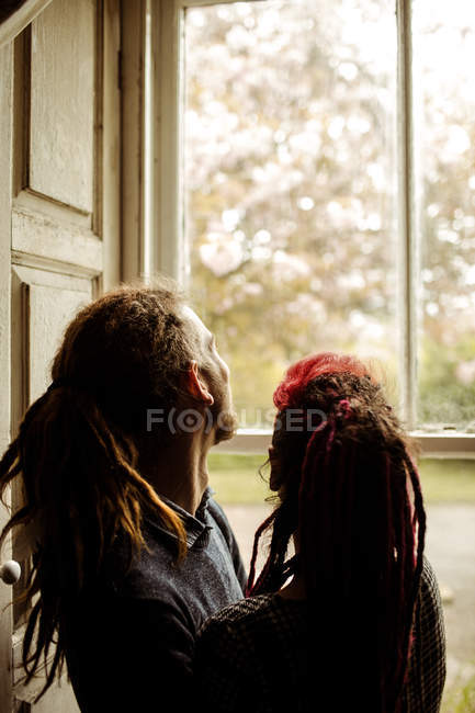 Vista lateral de la pareja de pie por la ventana en casa - foto de stock