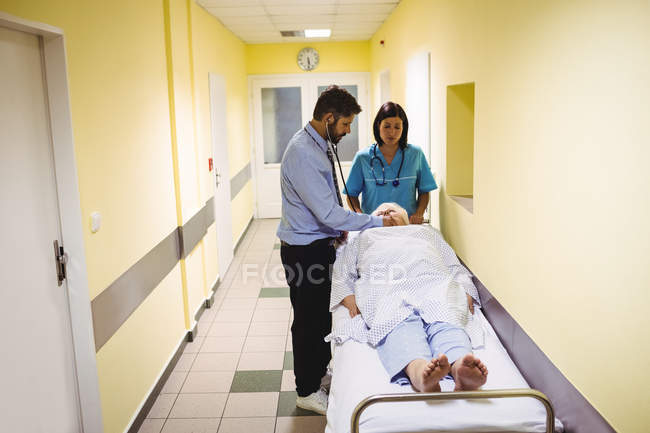 Médico examinando paciente mayor en corredor del hospital - foto de stock