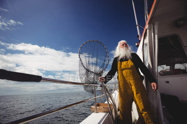 Fisherman holding fishing net and looking away from boat — Stock Photo
