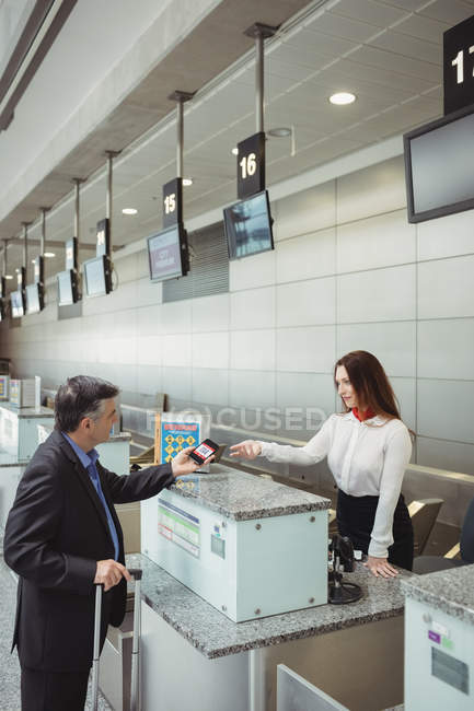 Бизнесмен, показывающий мобильный посадочный талон сотрудникам авиакомпании при регистрации на рейс — стоковое фото