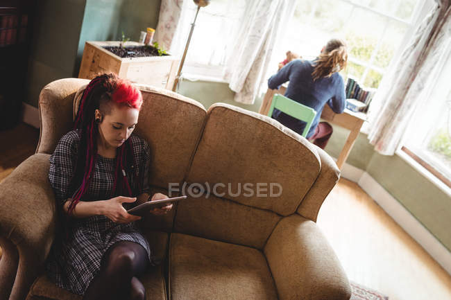 Mujer joven usando tableta digital mientras está sentada en el sofá en casa - foto de stock