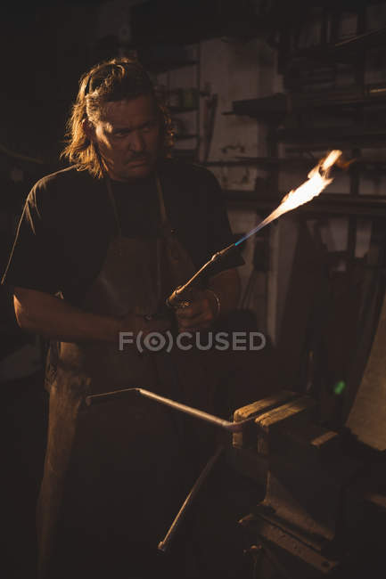 Forgeron tenant tuyau de soudage en atelier — Photo de stock