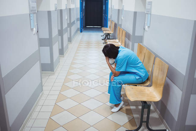 Enfermeira triste sentada em cadeira de madeira no corredor do hospital — Fotografia de Stock