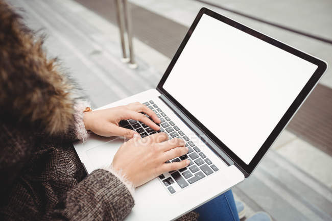 Обрізане зображення жінки, яка друкує на ноутбуці, сидячи на кроках — стокове фото