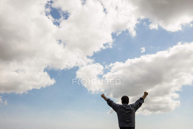 Vue arrière de l'homme les bras levés contre un ciel nuageux — Photo de stock