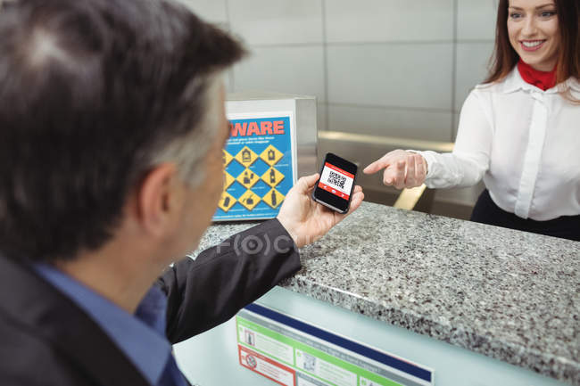 Empresario que muestra la tarjeta de embarque móvil al asistente de facturación de la aerolínea en el mostrador de facturación - foto de stock