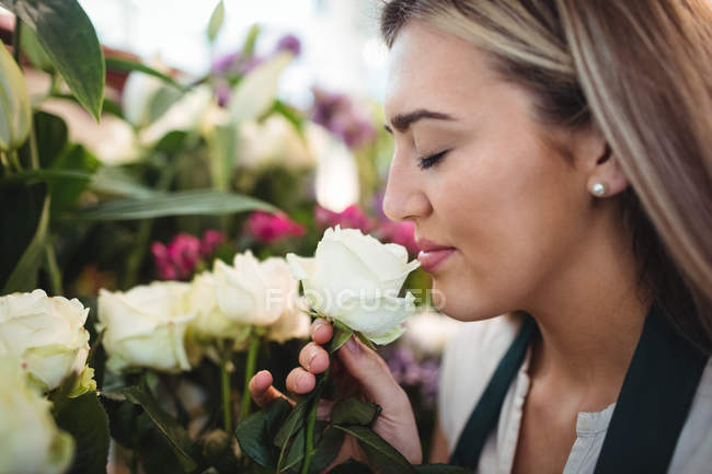 Primo piano di fiorista femminile che odora di fiore al suo negozio di fiori — Foto stock