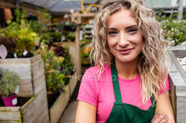 Retrato de florista femenina sonriendo en el centro del jardín - foto de stock