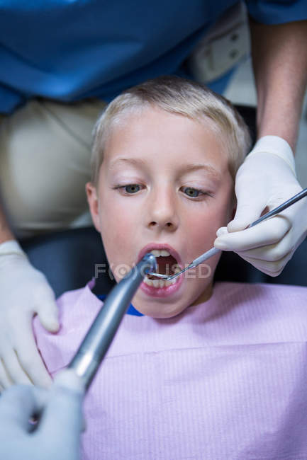 Dentista examinando a un paciente joven con herramientas en la clínica dental - foto de stock