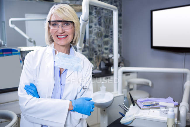 Портрет улыбающегося стоматолога, стоящего со скрещенными руками в стоматологической клинике — стоковое фото