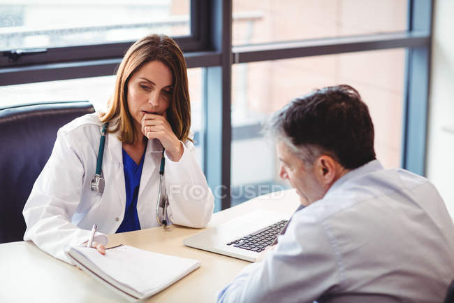 Female doctor at desk talking to patient in hospital — Stock Photo