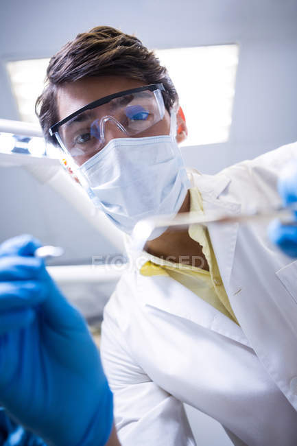 Dentista em máscara cirúrgica e óculos de proteção segurando ferramentas odontológicas na clínica odontológica — Fotografia de Stock