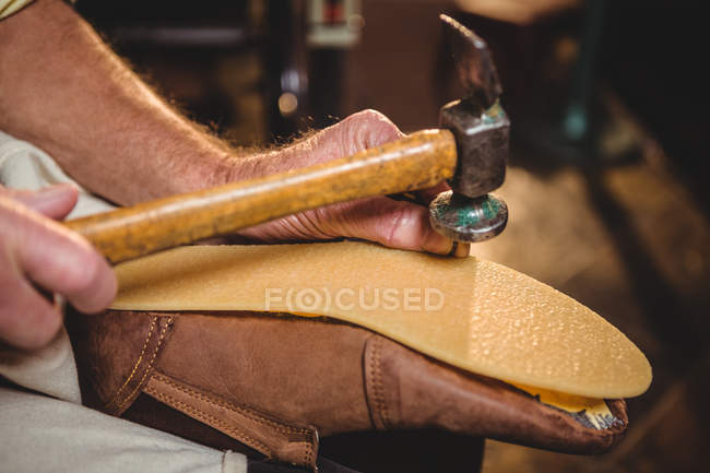 El primer plano del zapatero martillando el zapato en el taller - foto de stock