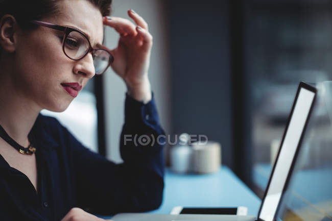 Mujer reflexiva usando el ordenador portátil en la mesa en la cafetería - foto de stock