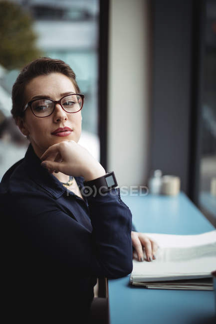 Pensativa mujer de negocios sentada junto a la mesa en la cafetería - foto de stock