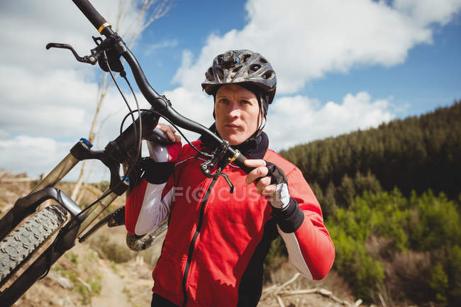 Vista frontal del ciclista llevando bicicleta en la montaña contra el cielo - foto de stock