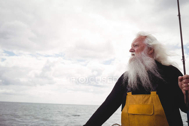 Вдумливий рибалка стоїть на човні і тримає рибальський стрижень — стокове фото