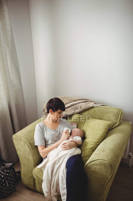 Vista de ángulo alto de la madre alimentando a su bebé en la sala de estar en casa - foto de stock