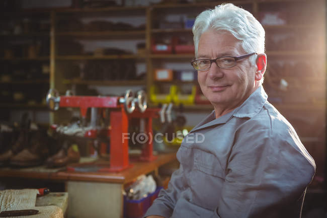 Портрет улыбающегося сапожника, сидящего в мастерской — стоковое фото