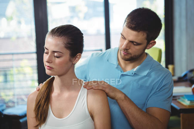 Fisioterapeuta masajeando hombro de paciente femenina en clínica - foto de stock