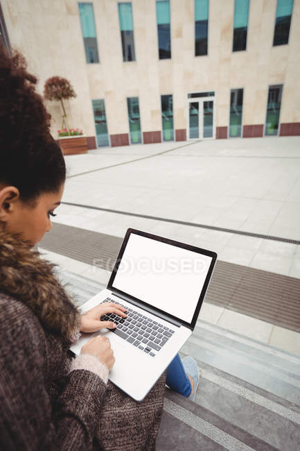 Жінка друкує на ноутбуці, сидячи на кроках — стокове фото
