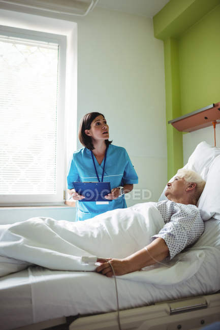 Krankenschwester interagiert über einen Bericht mit einem älteren Patienten im Krankenhaus — Stockfoto