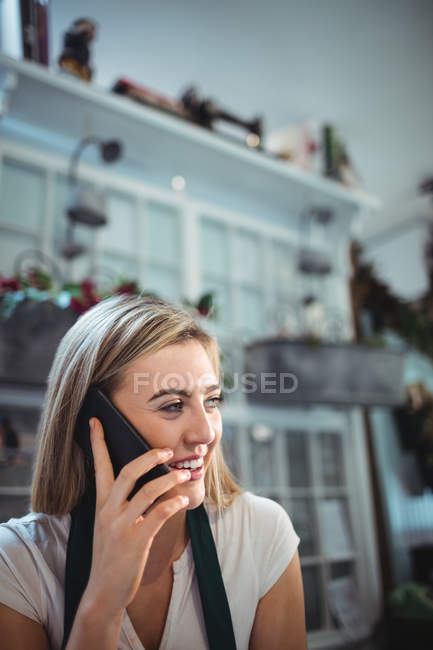 Девушка-флористка разговаривает по мобильному телефону в цветочном магазине — стоковое фото