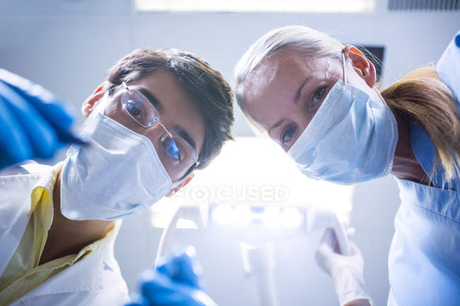 Odontoiatra e assistente odontoiatrico in maschere chirurgiche con strumenti odontoiatrici in clinica — Foto stock