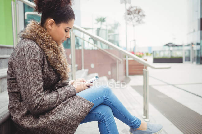 Seitenansicht einer Frau, die ihr Telefon benutzt, während sie auf den Stufen sitzt — Stockfoto