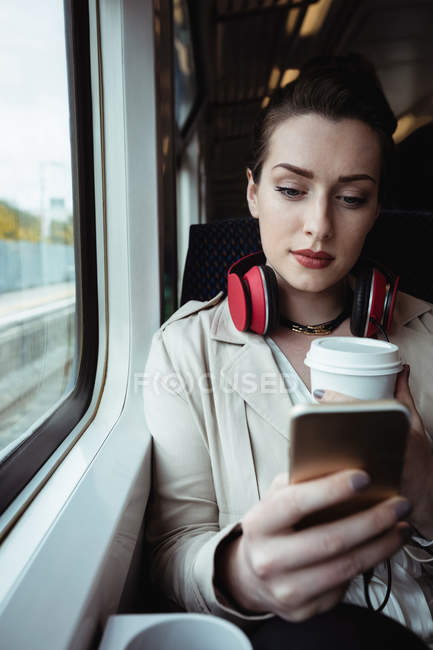 Jolie femme utilisant un téléphone portable assis par la fenêtre dans le train — Photo de stock