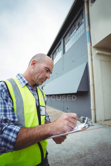 Bauarbeiter schreibt auf Klemmbrett vor Büro — Stockfoto