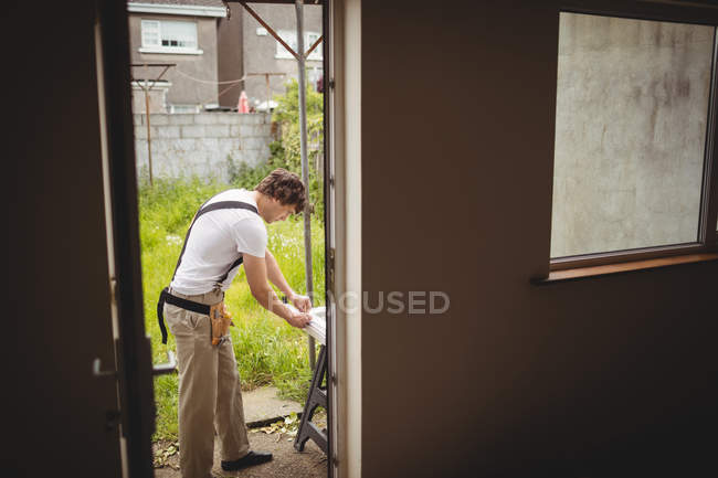 Тесляр вимірює дверну коробку зовні будинку — стокове фото