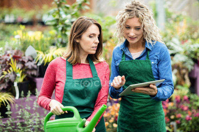 Duas floristas femininas usando tablet digital no centro de jardim — Fotografia de Stock