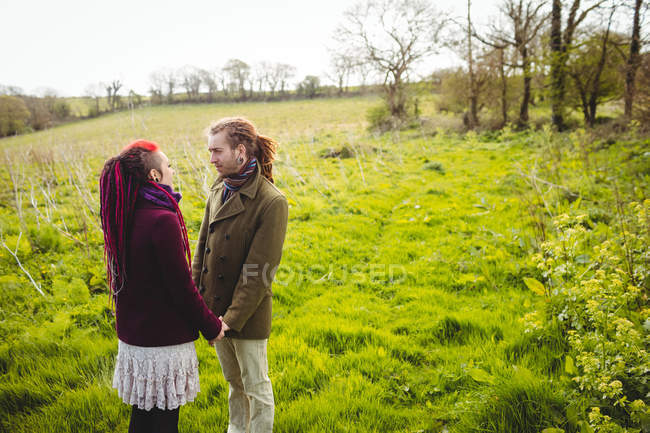 Hipster pareja cogida de la mano mientras está de pie en el campo de hierba en el parque - foto de stock