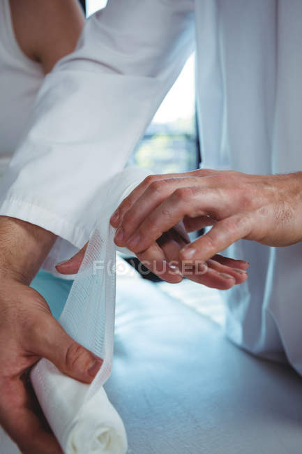 Image recadrée du thérapeute masculin mettant bandage sur la main du patient féminin en clinique — Photo de stock
