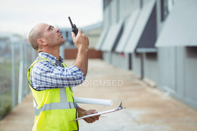 Construction worker talking on walkie-talkie outside office — Stock Photo