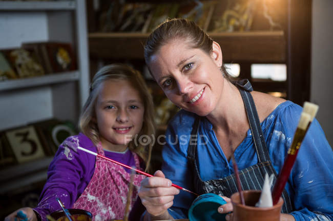 Portrait of female potter assisting girl in painting at pottery workshop — Stock Photo